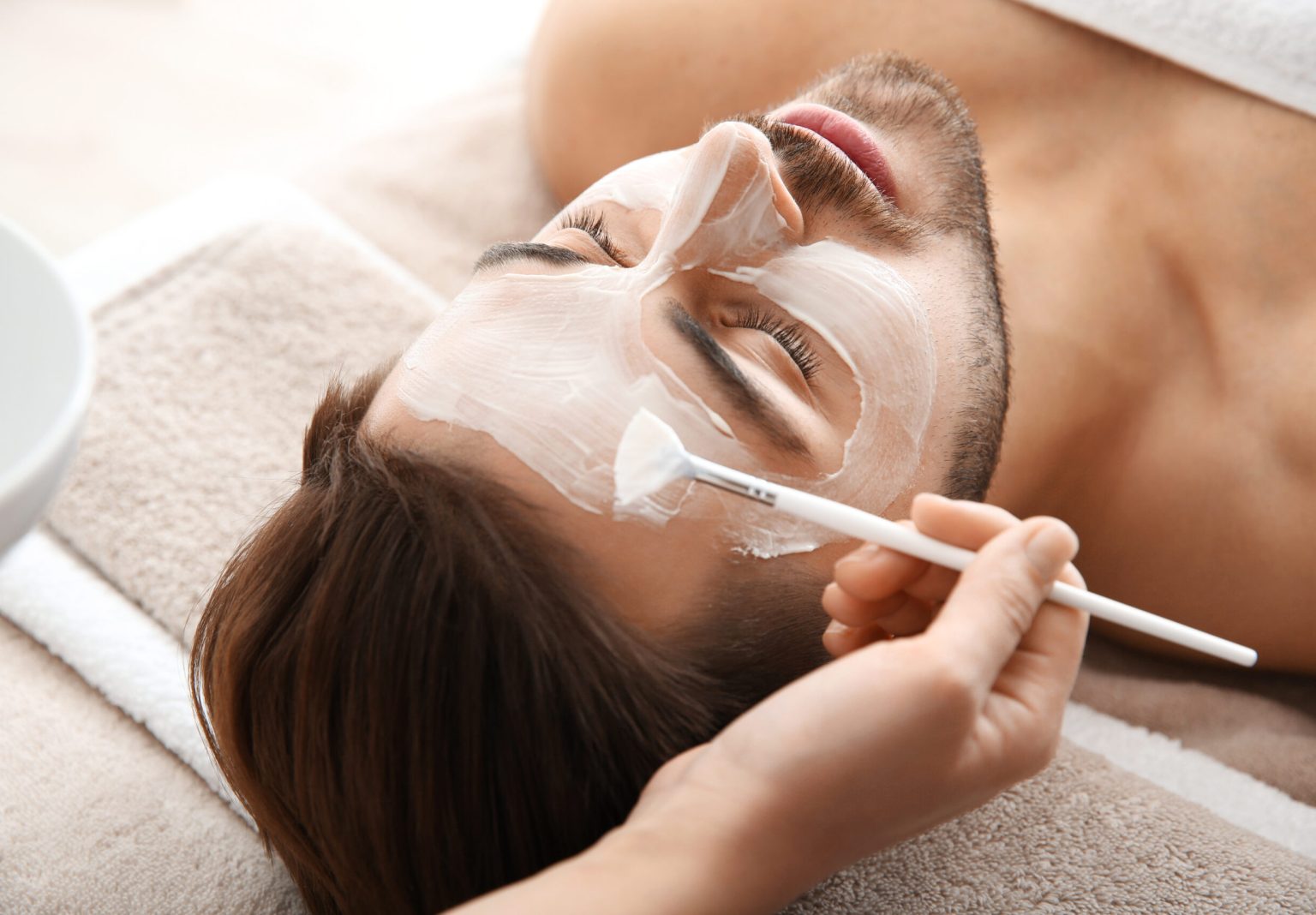 Cosmetologist applying mask on client’s face in spa salon mens skincare